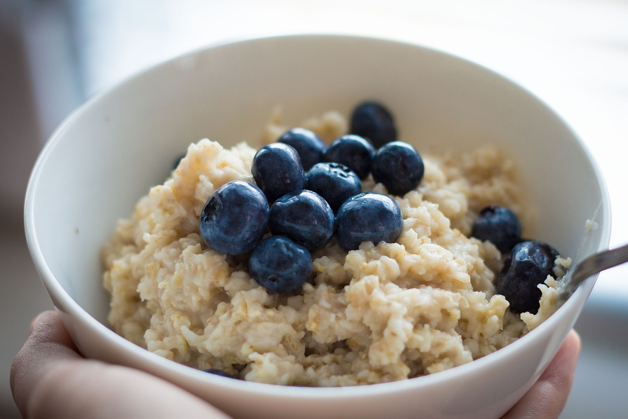 bowl of oatmeal resting on palm with blueberries inside of it