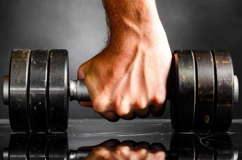 a man's hand gripping a dumbbell on the floor