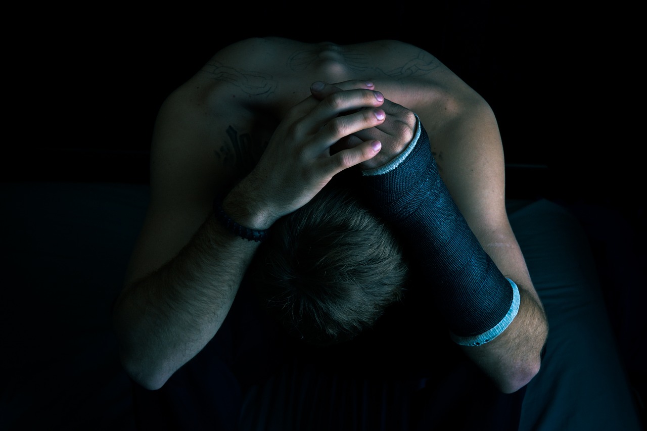a depressed man with leaned over with his hands behind his head with a cast on his arm